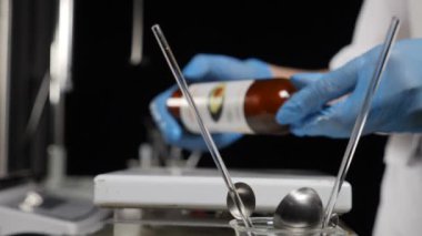 Modern kozmetik ve parfüm laboratuvarı. Eldivenli eller cam şişeyi ısıtma elementinin üstünde tutuyor. Bir kasenin içinde koyu yoğunlaştırılmış sıvı var. Ağır çekim. Tam Hd