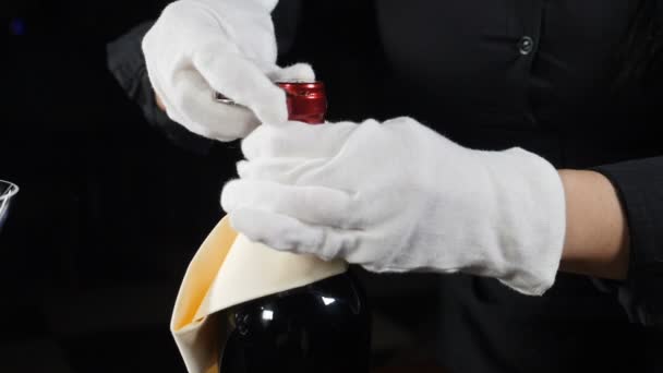 Un primo piano della bottiglia di vino che viene stappata. Cameriere in guanti bianchi girato su sfondo nero. la lamina di metallo viene tagliata. Al rallentatore. hd completo — Video Stock