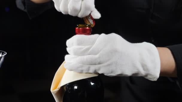 Butelka z winem jest niekorkowana.Close-up. Kelner w białych rękawiczkach nakręcony na czarnym tle. odcięcie folii. Zwolnij trochę. Pełny hd — Wideo stockowe