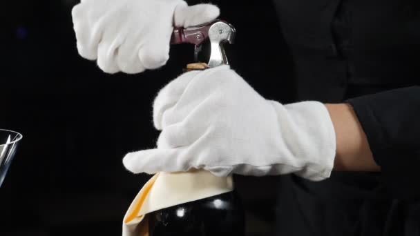 Concept de cave. Gros plan du sommelier ouvrant une bouteille de vin pour les visiteurs du restaurant. Serveur en gants blancs tourné sur fond noir. . Au ralenti. Full hd — Video