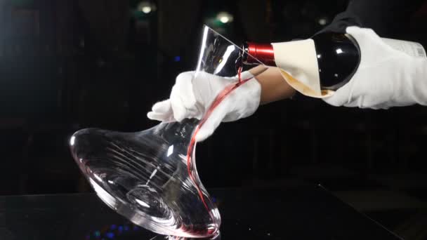 Skilled sommelier pouring red wine from bottle into decanter. Wine Degustation process in restaurant, close up. Hands in elegant white gloves on black background. Slow motion. Full hd — Stock Video