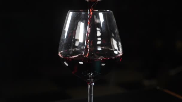 Wine being poured into wine glass on black background in slow motion. Pouring red wine from bottle neck into wine glass. Close-up shot. Full hd — Stock Video