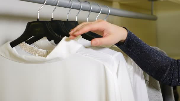 Imagem de close-up da mão feminina correndo em cabides de roupas Rack ferroviário e à procura de vestuário na loja de roupas. Conceito de compras. Filmagem 4K — Vídeo de Stock
