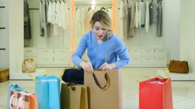 Alışveriş konsepti. Moda mağazasında alışveriş yapan kız etrafta kağıt torbalarla kameraya gülümsüyor. Kara Cuma ve Satış Konsepti. Satış mesajı kızların elinde. 4k video