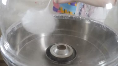 Pamuk helvayı pamuk helva makinesinde yuvarlayan bir kadın. Tatlı pamuk helva yapıyorum. Beyaz diş ipli pamuk helva makinesi. İnsanlar tatilde çocuklar için pamuk şeker yapar. Ağır çekim. Tam