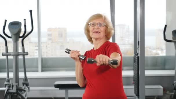 Ενεργός συνταξιούχος γυναίκα με κουδούνια στο γυμναστήριο. Ενεργός και ευτυχισμένος παλιά έννοια χρόνια. Θετικός συνταξιούχος που κάνει ελαφρές ασκήσεις με αλτήρες στο γυμναστήριο. Βίντεο 4k — Αρχείο Βίντεο