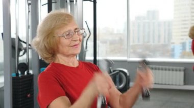 Spor salonunda halterlerle hafif egzersizler yapan pozitif emekliler. Spor salonunda koltuk değnekleriyle emekli bir kadın. Aktif ve mutlu eski yıllar konsepti. 4k video
