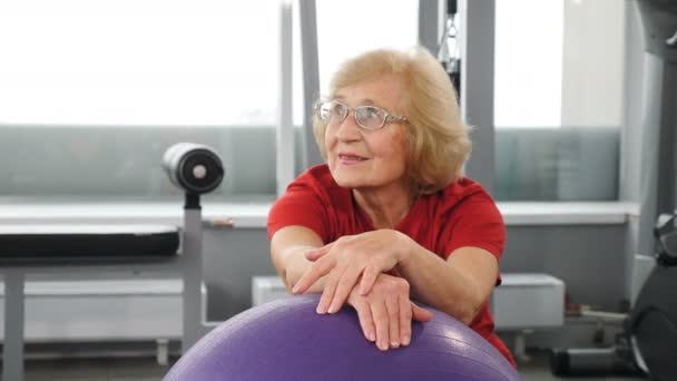在健身房参加健身球的退休愉快女人的画像。健康而活跃的老妇人。活跃的老年人。老太太在健身室。4k镜头 — 图库视频影像