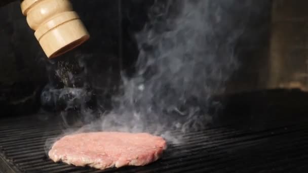 Video di slow motion. Hamburger che cucina. Primo piano di hamburger crudo patty su una piastra come pepe viene spruzzato sulla parte superiore. Il vapore si alza. hd completo — Video Stock