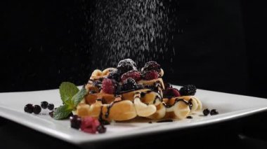Sugar powder being poured over waffle on black background in slow motion. delicious sweet dessert concept. Full hd