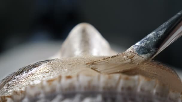 Top zicht op jonge aantrekkelijke vrouwelijke klant krijgen schoonheid gezichtsbehandeling in schoonheidskliniek. liftend effect op het gezicht van de klant. Cosmetoloog het aanbrengen van gouden masker met een borstel. Een close-up. 4 k video — Stockvideo