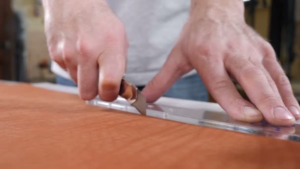 Hands of skilled leather craftsman using plastic pattern and leather knife to cut out part from piece of red leather, close-up shot. Industrial knife man cuts the work piece from the skin. 4 k footage — Stock Video