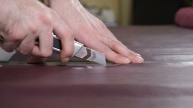Manually cutting leather during craft manufacturing goods. Workshop of skinner, close-up shot showing hands of master and production process. Cutting of detail of leather accessories and bags on a
