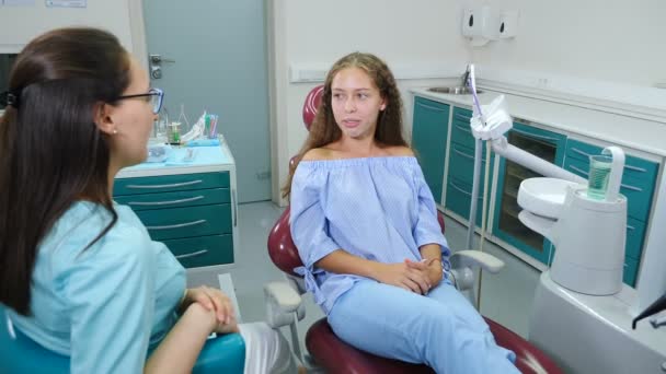 En la clínica dental. concepto de ortodoncia. En consulta con el doctor ortodoncista. Una chica guapa con frenillos en los dientes en el consultorio del dentista. Dientes blancos y sanos. Disparo de 4 k — Vídeo de stock