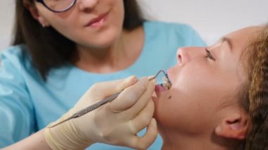 Gülümseyen kadın ortodontist dişçi muayenehanesinde çocuğu muayene ediyor. Yakın plan. Modern diş kliniğinde dişlerinde diş teli olan güzel bir kız. Ortodontik tedavi. Diş telli dişler. Isırık düzeltmesi