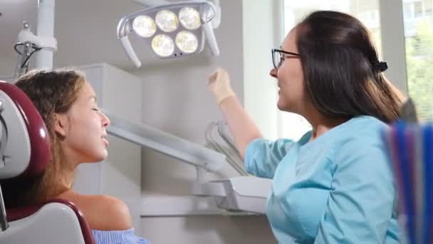 Vista superior de la mujer joven pacienteen silla dental. Doctor arreglando la luz de la lámpara antes del tratamiento. Primer plano. El dentista enciende la luz de la lámpara dental. Dentista en el trabajo. Concepto de dentista moderno. 4 k imágenes — Vídeos de Stock