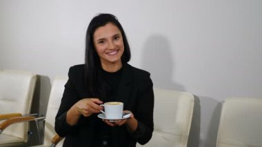 Happy girl drinking coffee and relaxing in office smiling and looking at camera. smiling woman enjoying gorgeous coffee at office waiting for appointment. Girl waiting for health care procedure in