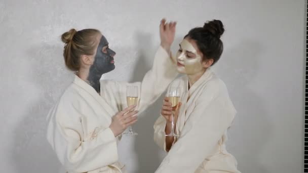 Retrato de amigas felices y emocionadas celebrando la fiesta con copas de champán en el salón de belleza. Mujer bastante joven que tiene tratamiento de exfoliación cosmética facial en el spa de bienestar. Cuidado facial de la piel y — Vídeos de Stock