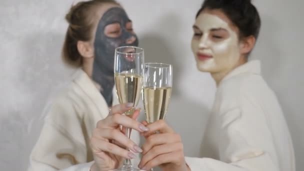 Cheerful beautiful caucasian young female best friends wearing white bathrobes holding glasses with champagne laughing at camera, two happy playful ladies gather on spa pajama party or bridal shower — Stock Video