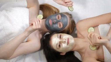 Top view on Joyful young girls friends having fun while doing cucumber mask in light beauty salon. Wellness, spa, skincare and bachelorette party or bridal shower concept. 4k video