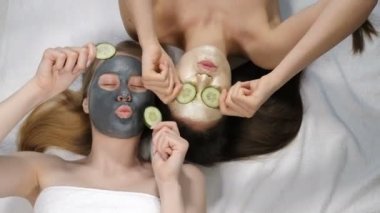 Top view on Joyful young girls friends having fun while doing cucumber mask in light beauty salon. Wellness, spa, skincare and bachelorette party or bridal shower concept. 4k video
