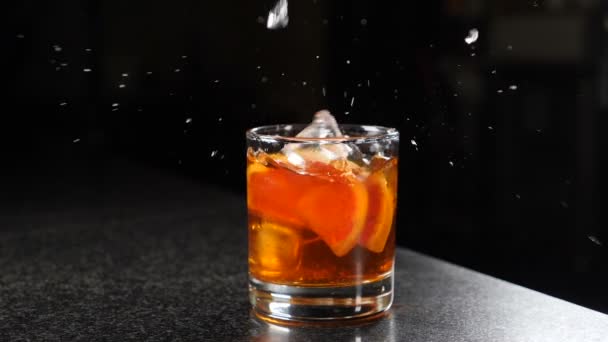 Falling ice cubes into glass with spirit beverage with splashes shot on black background. Slow motion. fun, nutrition and drink concept. Party with splashes and drops of alcohol. Feast all night. Full — Wideo stockowe