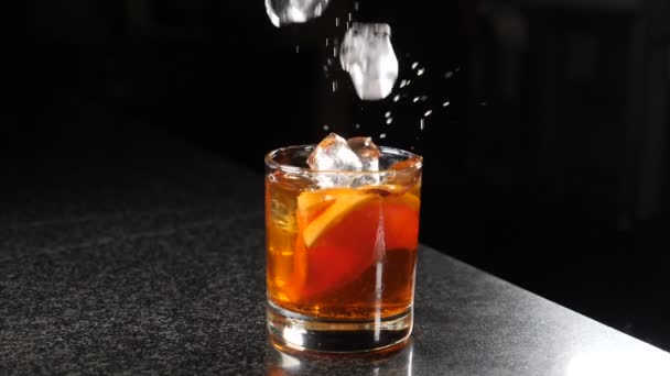 Falling ice cubes into glass with spirit beverage with splashes shot on black background. Slow motion. fun, nutrition and drink concept. Party with splashes and drops of alcohol. Feast all night. Full — Stok video