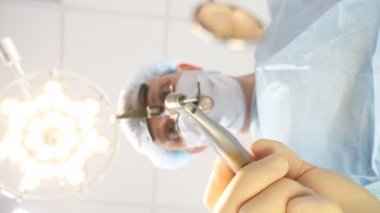 Diş kliniğindeki hastanın durumu. Beyaz ağız maskeli doktor elinde tıbbi aletlerle Hasta 'ya yaklaşıyor ve tedaviye başlıyor. Korumacı erkek dişçi üniformasının portresi