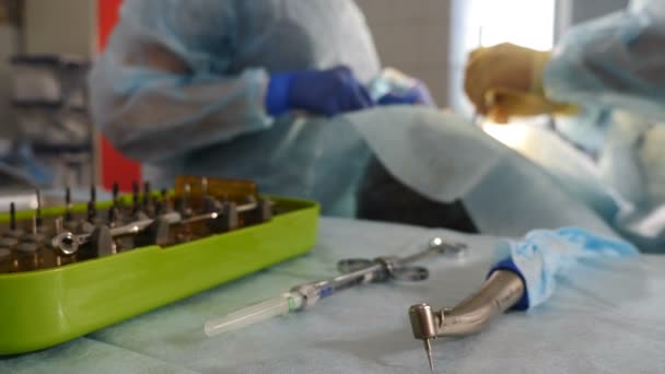 Traitement dentaire flou tiré à travers les outils sur la table. Dentiste et infirmière au travail, gros plan. Le patient subit une opération chirurgicale médicale et un traitement de la cavité buccale à la dentisterie moderne. Vidéo 4 k — Video