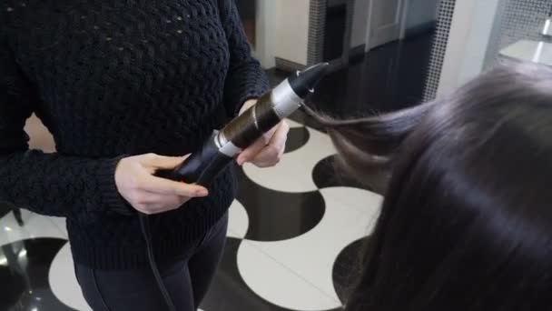 Gros plan sur les cheveux bouclés des coiffeuses à l'aide de fer à repasser. Processus de friser les cheveux longs avec des pinces à cheveux dans le studio de beauté moderne. Coiffeur faisant coiffure élégante. Macro. Images 4k — Video