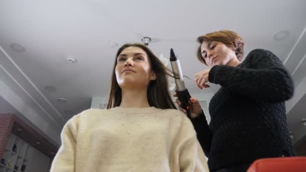 Концепция салона красоты. Молодая женщина во время выпрямления волос. Парикмахер, использующий утюг и расческу для женской прически в парикмахерской. Парикмахер создает женскую прическу с щипцами. 4k видео — стоковое видео