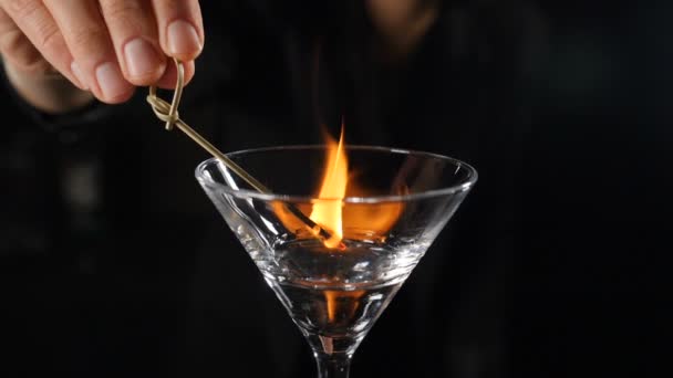 Barman femelle mettre le feu avec bâton brûlant sur cocktail d'alcool au ralenti. Allumage de feu sur boisson avec de l'alcool. Flammes en verre transparent. Comptoir de bar sur fond noir. Vidéos HD complètes — Video