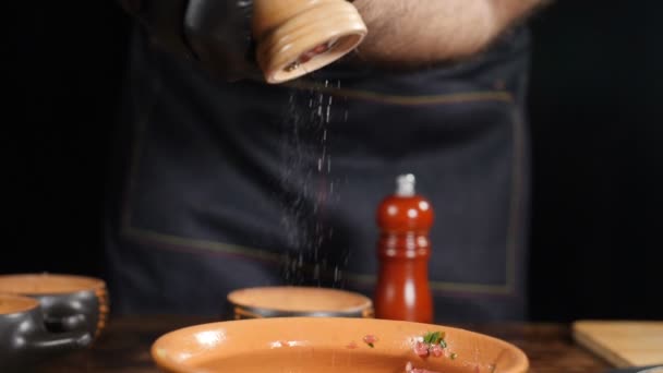 Zbliżenie strzał szefa kuchni za pomocą drewnianego młyna, aby dodać trochę soli do naczynia, sól spada w zwolnionym tempie, mielenie soli, za pomocą naczynia kuchennego. Film z żywnością. Pełny hd — Wideo stockowe