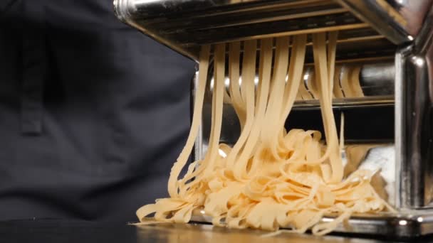 Traditional italian homemade pasta being made on machine for cutting dough. Slow motion food footage of Fresh spaghetti pasta coming out of pasta machine, close-up. Chef use pasta cutting machine — Stock Video