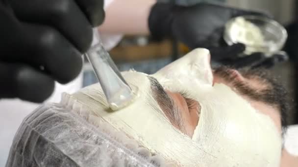 Concepto de salón de belleza y spa para hombres. esteticista aplicando mascarilla facial cosmética con pincel. Terapia de spa para hombre guapo recibiendo tratamiento facial rejuvenecedor. cosmetología y concepto de belleza — Vídeos de Stock