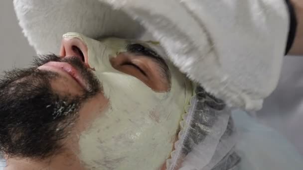 Imagem de perto do procedimento facial de beleza masculina. Eliminar a máscara hidratante. Cosmetologist com mãos enluvadas fazendo tratamento de beleza. Filmagem 4k — Vídeo de Stock