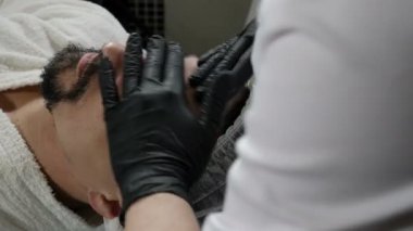 Güzellik salonu ve erkekler için kaplıca kavramı. Güzellik uzmanı eldivenli ellerle maske takıyor. Yakışıklı bir adam için spa terapisi. Yenilenen yüz bakımı. 4k görüntü