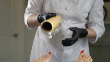 Cosmetic procedure body wraps. Beautician in black gloves covers with anti-cellulite cellophane female legs in modern cosmetology centre. Moisturizing body mask and body wrap. 4k footage