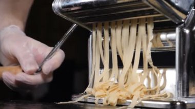 Hamur kesmek için el makinesinde geleneksel İtalyan ev yapımı makarna yapılıyor. Makarna makinesinden çıkan taze spagetti makarnasının yavaş çekim görüntüleri, yakın plan. Şef makarna kesme makinesi kullanıyor.