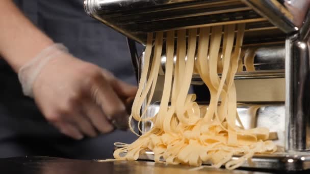 Hamur kesmek için el makinesinde geleneksel İtalyan ev yapımı makarna yapılıyor. Makarna makinesinden çıkan taze spagetti makarnasının yavaş çekim görüntüleri, yakın plan. Şef makarna kesme makinesi kullanıyor. — Stok video