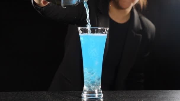 Жінка-бармен робить синій крижаний коктейль на чорному тлі. Перукар виливає яскраво-синій лікер у склянку, наповнену льодом. Атмосфера нічного клубу. Темний лічильник. Крупним планом. Повільний рух. Повний HD — стокове відео