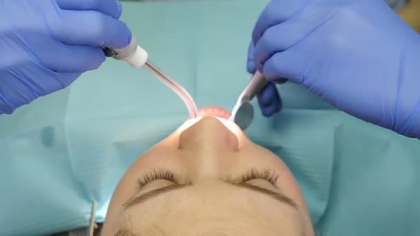 Концепция стоматологии. Вид сверху на стоматолога, осматривающего маленькую пациентку. Кооперация врача и ассистента. Стоматолог держит стоматологические инструменты. В современном стоматологическом кабинете. 4 k видео — стоковое видео