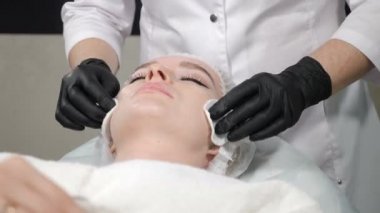 Beauty concept, Close-up shot of female getting facial cleaning procedure in salon. Beautician wiping client skin face with cotton pads. 4 k video