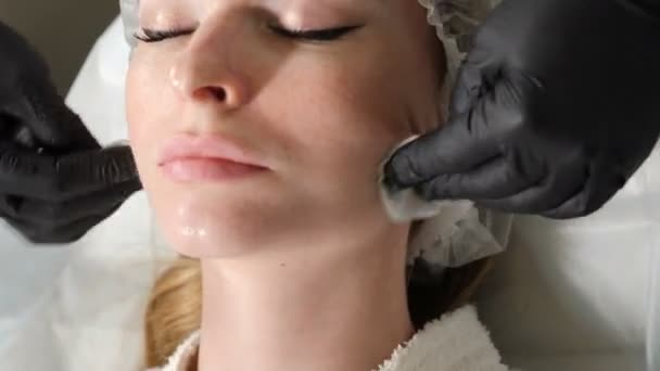 Un primo piano di una donna che fa la pulizia del viso nel salone di bellezza. Estetista pulire il viso della pelle del cliente con batuffoli di cotone. 4K video — Video Stock