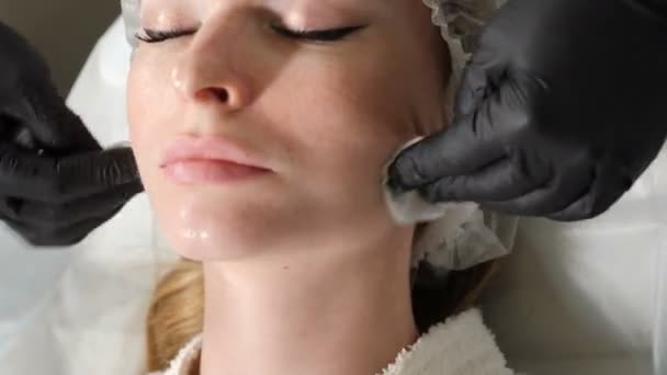 Close-up shot of female getting facial cleaning procedure in beauty salon. Beautician wiping client skin face with cotton pads. 4 k video — Stok video