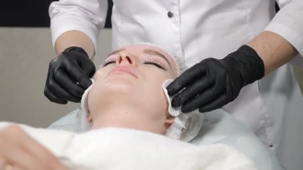 Концепція краси, крупним планом знімок жіночої процедури очищення обличчя в салоні. Косметолог протирає шкіру клієнта ватними подушечками. 4K відео — стокове відео