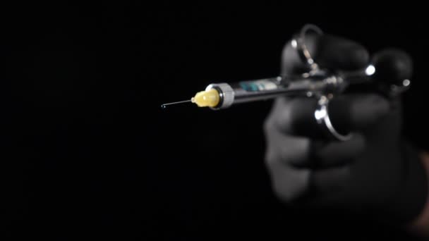 Zbliżenie zdjęcia dentysty trzymającego strzykawkę ze środkiem znieczulającym na czarnym tle. Medycyna, lekarz i koncepcja opieki zdrowotnej. Ręka dentysty w czarnej rękawiczce strzykawka trzymająca ze znieczuleniem Wypuszczanie leku — Wideo stockowe