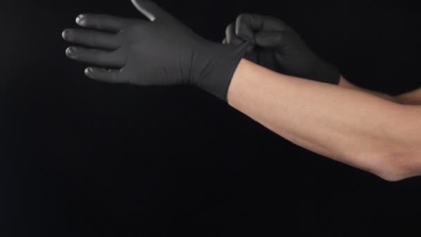 Mężczyzna lekarz zakłada czarne rękawice ochronne przed zabiegiem strzał na czarnym tle. filmik o ruchu maciory. Przenoszenie męskich rąk zakładanie egzaminów lub rękawic medycznych. Pełny hd — Wideo stockowe