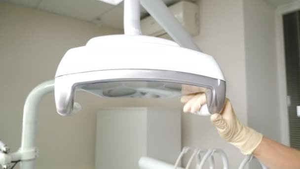 Fogorvos kezdő kezelés, csökkenti a fogászati lámpa, és bekapcsolja. Hivatásos fogorvosi rendelő. Közelkép. A fogorvosi műtő tele van modern felszereléssel. kézi állító felső fogászati vagy — Stock videók