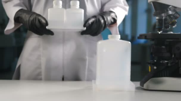 Moderní laboratorní koncept. Vědec v černé rukavici uvedení bílé plastové lahve kontejnery s mikroskopem v pozadí. Kopírovat místo pro poznámku. Záběry 4 k — Stock video